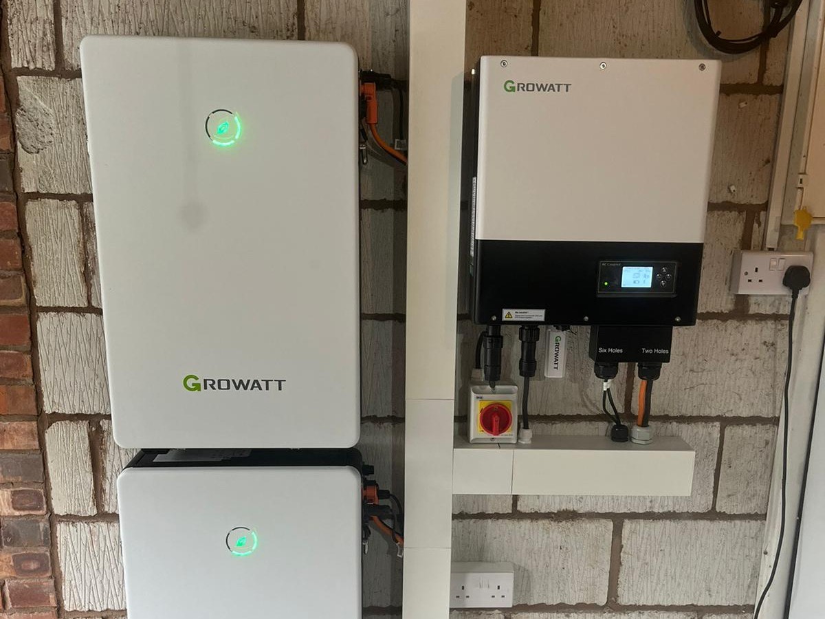An L&R battery installation: two Growatt battery modules beside a Growatt inverter and its isolator switch on a garage wall