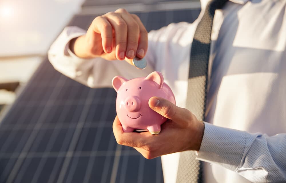A piggy bank in the foreground, solar panels in the background.