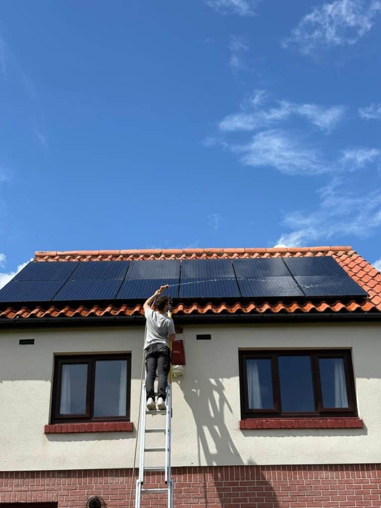 L&R engineer on a ladder cleaning black solar panels on a tiled roof