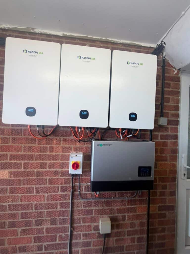 Three wall-mounted solar batteries above a hybrid inverter and isolator switch