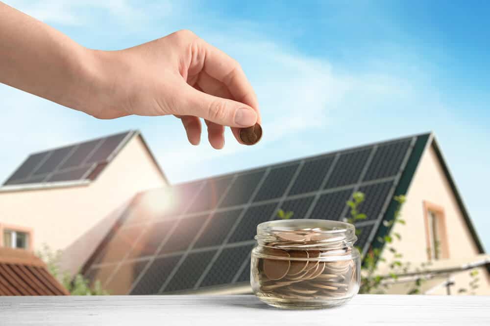 A jar of coins, with solar panels on a rooftop in the background.